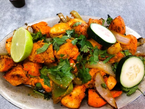 A platter of spiced roasted vegetables, including potatoes, onions, and cucumbers, garnished with fresh cilantro and lime.