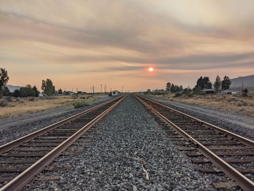A view of railway tracks stretching into the distance under a smoky sky with a setting sun.