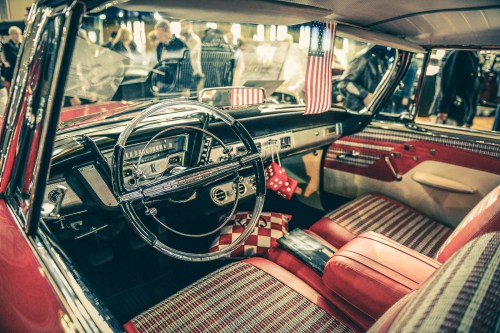 Vintage car interior featuring red and white checkered upholstery, a classic steering wheel, and American flags.