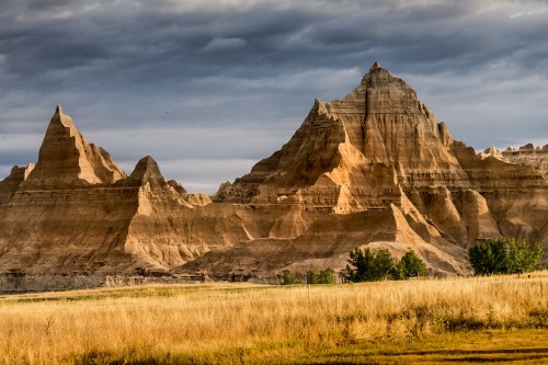 A rugged landscape featuring towering rock formations under a cloudy sky, with golden grass in the foreground.