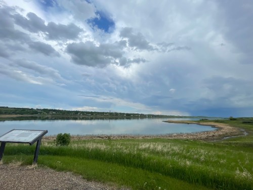 A serene lake surrounded by green grass and cloudy skies, with a signpost in the foreground.