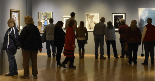 Visitors explore an art gallery, admiring various framed artworks on the walls.