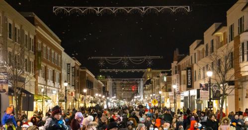 A bustling street at night filled with people, decorated with festive lights and holiday decorations overhead.