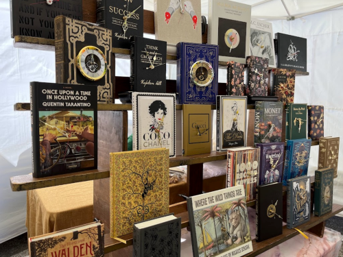 A display of various decorative books on a wooden table, featuring titles by famous authors and brands.