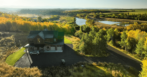 Aerial view of a house surrounded by vibrant autumn trees and a serene river in the background.