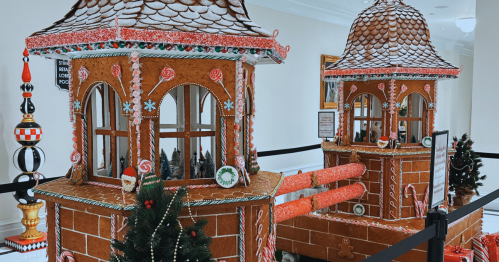 Two large gingerbread houses decorated with candy, surrounded by festive decorations in a bright indoor space.