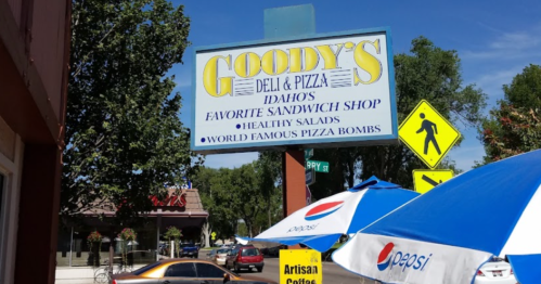 Sign for Goody's Deli & Pizza, advertising healthy salads and world-famous pizza bombs, with outdoor seating visible.