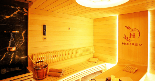 A warm wooden sauna interior with a bench, a bucket, and a logo on the wall, creating a relaxing atmosphere.