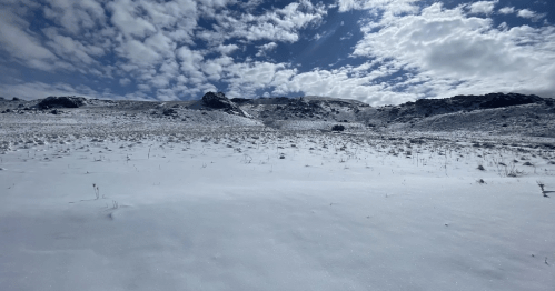 A snowy landscape with rolling hills under a partly cloudy sky.