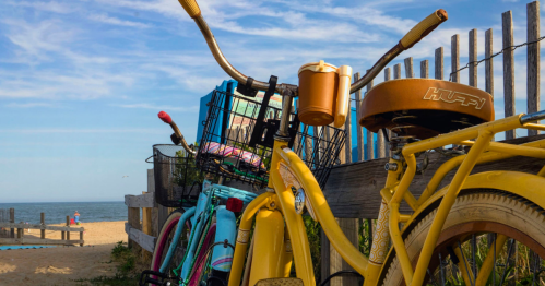 A row of colorful bicycles parked by a beach, with a blue sky and ocean in the background.