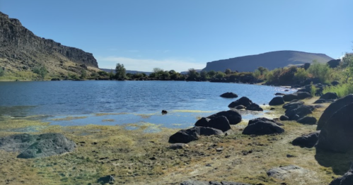A serene lake surrounded by rocky shores and hills under a clear blue sky.