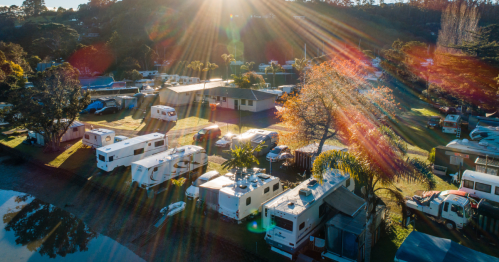 Aerial view of a campsite with RVs and trailers, surrounded by trees and sunlight streaming through.