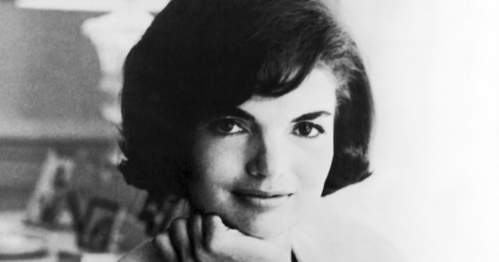 Black and white portrait of a woman with dark hair, resting her chin on her hand, looking thoughtfully at the camera.