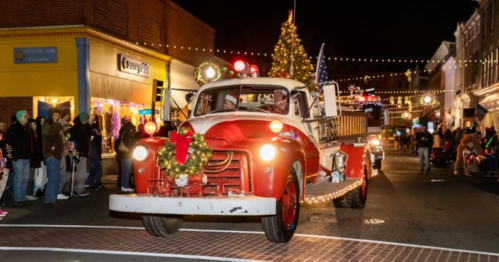 A vintage red fire truck decorated with lights and a wreath drives through a festive night parade.