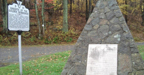 A stone monument and historical marker in a wooded area, surrounded by autumn foliage.