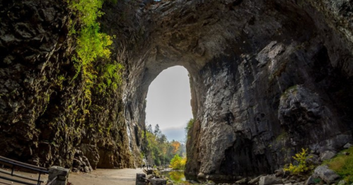 A large rock archway surrounded by steep cliffs and greenery, with a pathway leading through the opening.