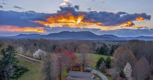 A scenic view of mountains at sunset, with colorful clouds and trees in bloom in the foreground.