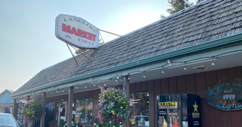 Exterior of Langlois Market & Deli, featuring a sign, hanging lights, and flower baskets. Established in 1949.