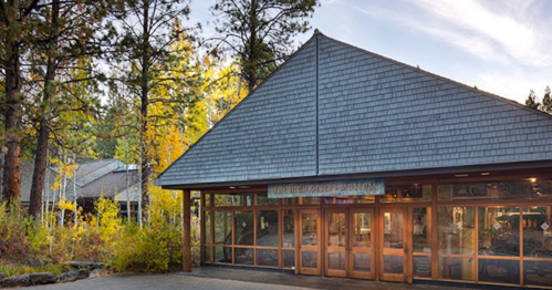 Exterior of the High Desert Museum, surrounded by trees and autumn foliage, with a clear sky above.