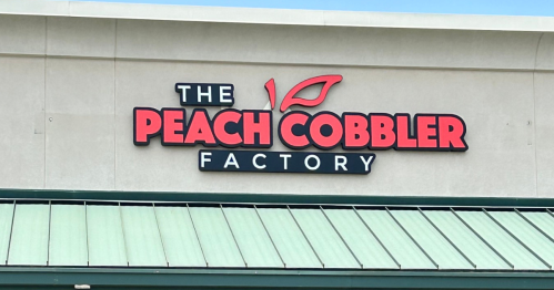 Sign for "The Peach Cobbler Factory" on a building with a green roof.