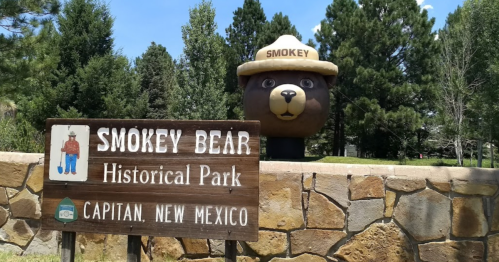 Sign for Smokey Bear Historical Park in Capitan, New Mexico, with a large Smokey Bear statue in the background.