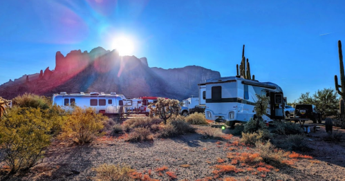 A scenic view of RVs parked in a desert landscape with mountains and a bright sun in the background.