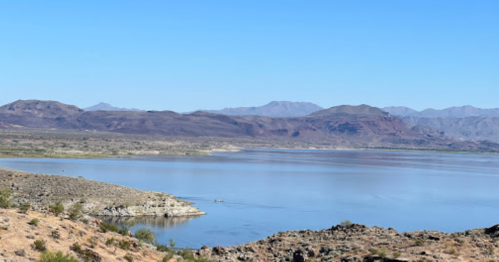 A serene landscape featuring a calm lake surrounded by mountains and clear blue skies.