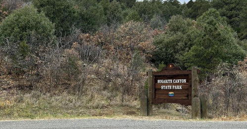 Sign for Sugarite Canyon State Park surrounded by trees and shrubs, with a gravel road in the foreground.