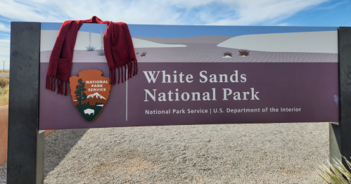 A sign for White Sands National Park, featuring a red scarf draped over it against a blue sky.