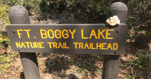 Sign for Ft. Boggy Lake Nature Trail trailhead, featuring yellow lettering on a dark background, with a small rock on top.