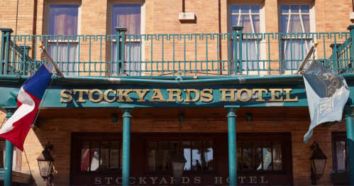 Signage of the Stockyards Hotel, featuring flags and a brick facade, with windows above.