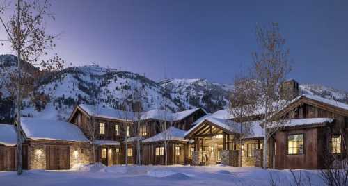 A cozy mountain lodge surrounded by snow, with a backdrop of majestic mountains under a twilight sky.