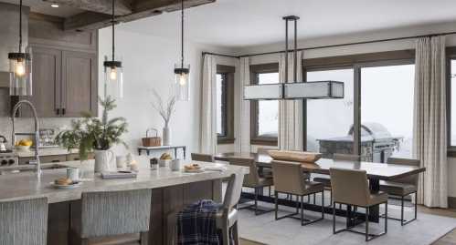 Modern kitchen and dining area with a large table, pendant lights, and large windows overlooking a snowy landscape.