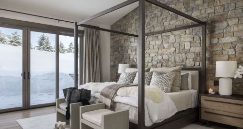 Cozy bedroom with a four-poster bed, stone wall, and large windows overlooking a snowy landscape.