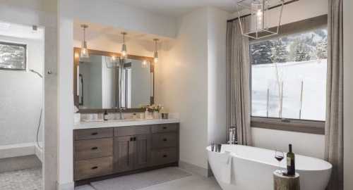 Modern bathroom featuring a freestanding tub, double vanity, and large window with a snowy view. Elegant lighting fixtures.