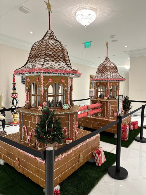 A festive gingerbread house display with two towers, decorated with candy, trees, and holiday ornaments.