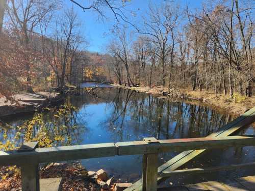 A serene river scene with autumn trees reflecting in the water under a clear blue sky.