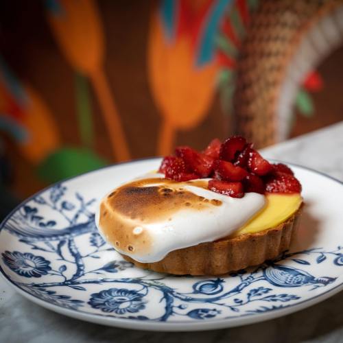 A beautifully plated tart with a toasted meringue topping and fresh strawberries on a decorative blue and white plate.