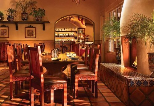 Cozy restaurant interior with wooden tables, chairs, and warm lighting, featuring decorative plants and tiled accents.