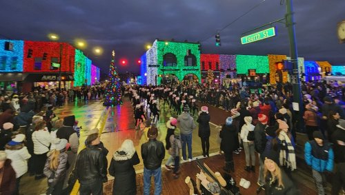 A festive street scene with colorful holiday lights, a parade, and a large crowd enjoying the celebration.
