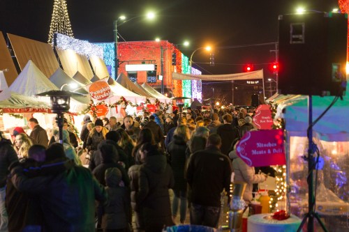 A bustling holiday market at night, with festive lights, stalls, and crowds enjoying the seasonal atmosphere.