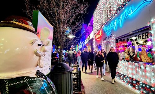A festive street scene with colorful lights, people walking, and a whimsical statue in the foreground.