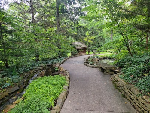 A winding path through lush greenery, leading to a small wooden structure surrounded by trees and a gentle stream.