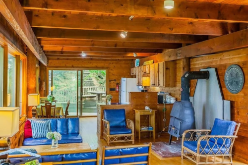 Cozy wooden cabin interior with a living area, kitchen, and large windows overlooking nature.