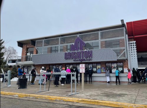 A crowd of people waiting outside the Brighton ski area building on a snowy day.