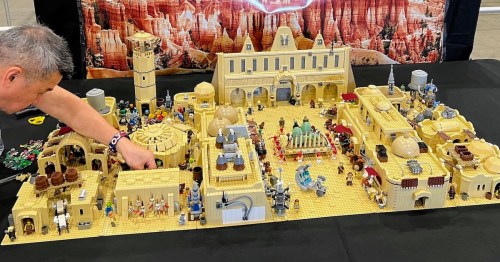 A detailed LEGO scene depicting a desert town with various buildings and figures, set on a black table.