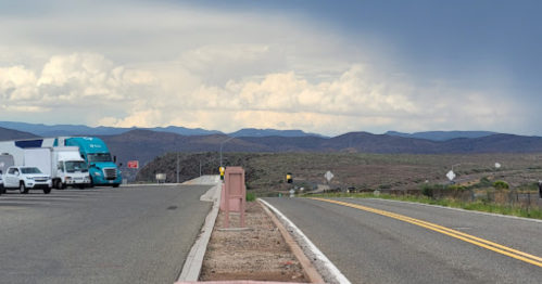 A highway scene with trucks and cars, mountains in the background, and a cloudy sky overhead.