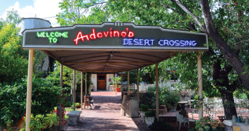 Colorful sign reading "Welcome to Andovino's Desert Crossing" at an entrance surrounded by greenery.