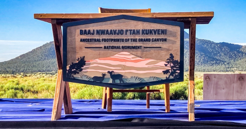 A wooden sign at a table reads "Baaj Nwaavjo I'tah Kukveni: Ancestral Footprints of the Grand Canyon National Monument."