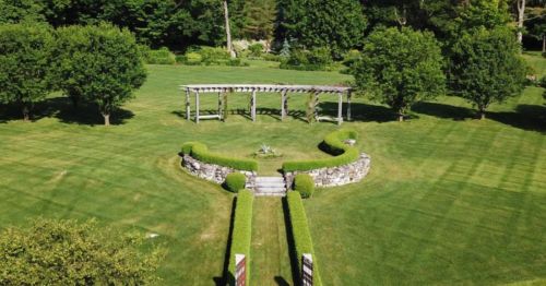 Aerial view of a landscaped garden featuring neatly trimmed hedges, a stone wall, and a wooden pergola.